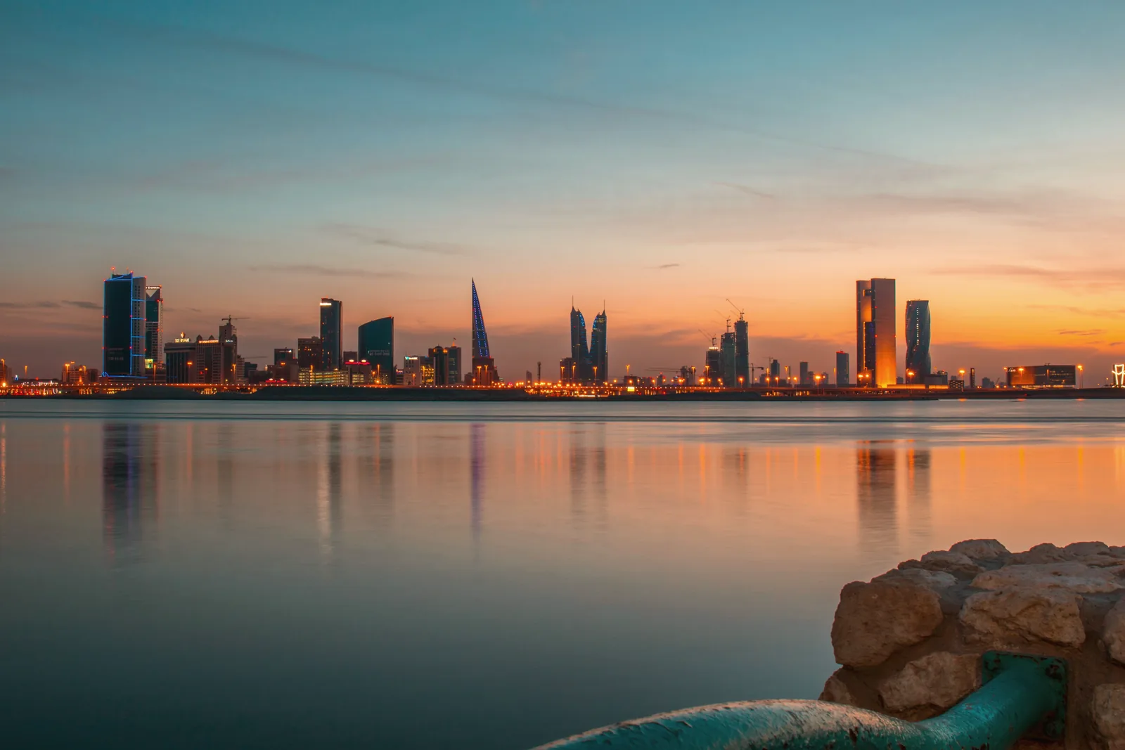 The Manama skyline at sunset over still water